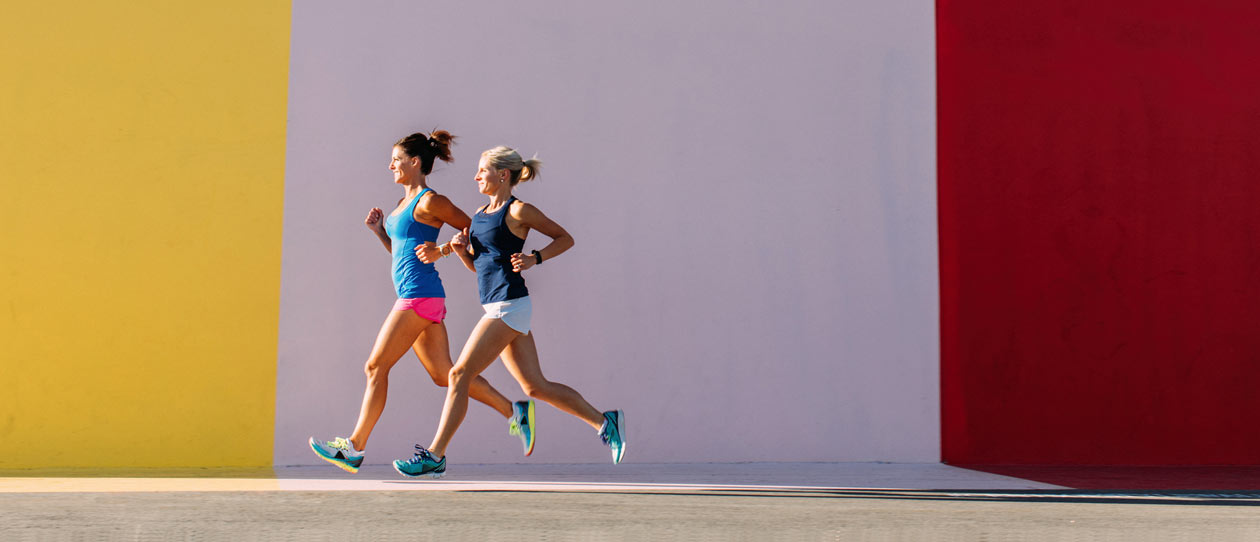 Two middle aged women running in front of a brightly covered wall