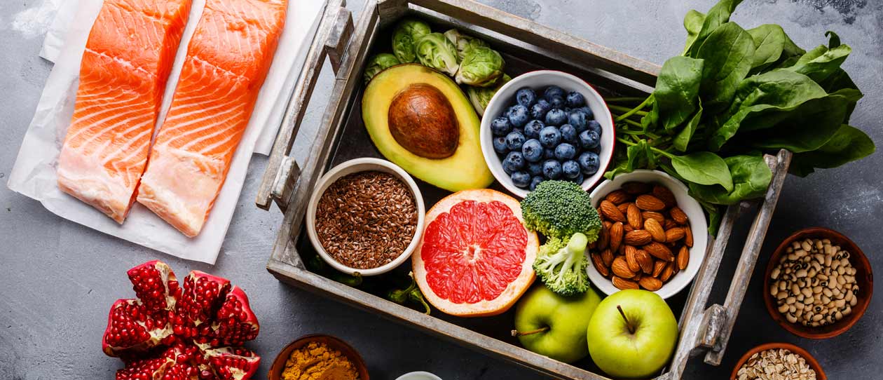 Flat lay of healthy foods including salom, pomegranate, blueberries, avocado, nuts, leafy greens and appples