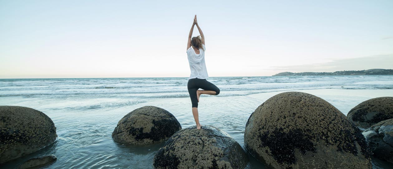 Young woman exercises doing yoga on a boulder at Moeraki boulders