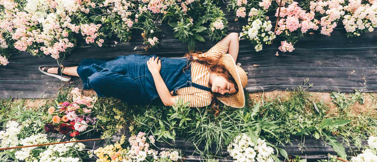 Smiling woman lying on a timber bench surrounded by flowers