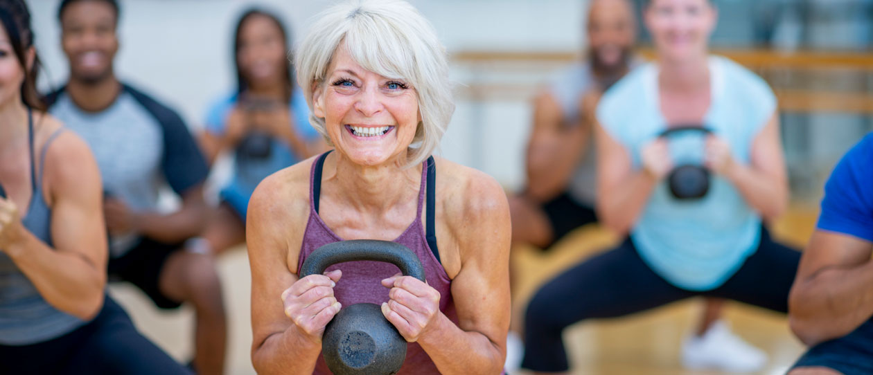 Mature woman squatting with a kettlebell in a gym class