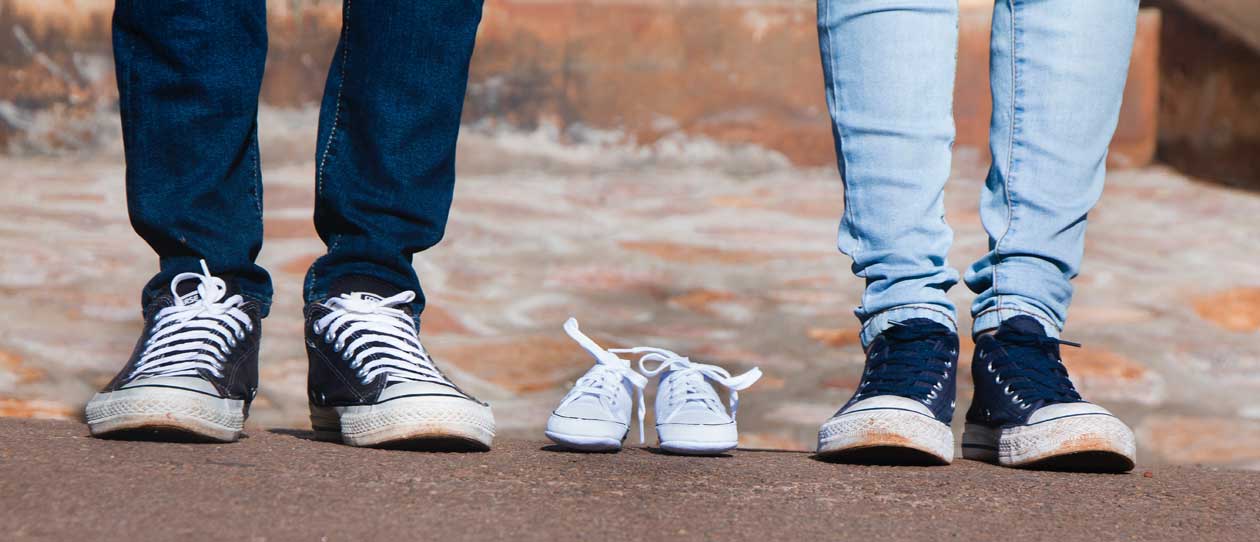 Pair of baby, grey low-top shoes between a couple wearing jeans