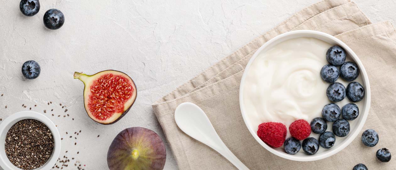 Natural healthy superfood fermented yogurt with blueberry, figs, chia seeds and raspberry in white bowl on light gray table