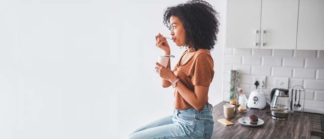 Young woman sitting on the kitchen bench eating yoghurt