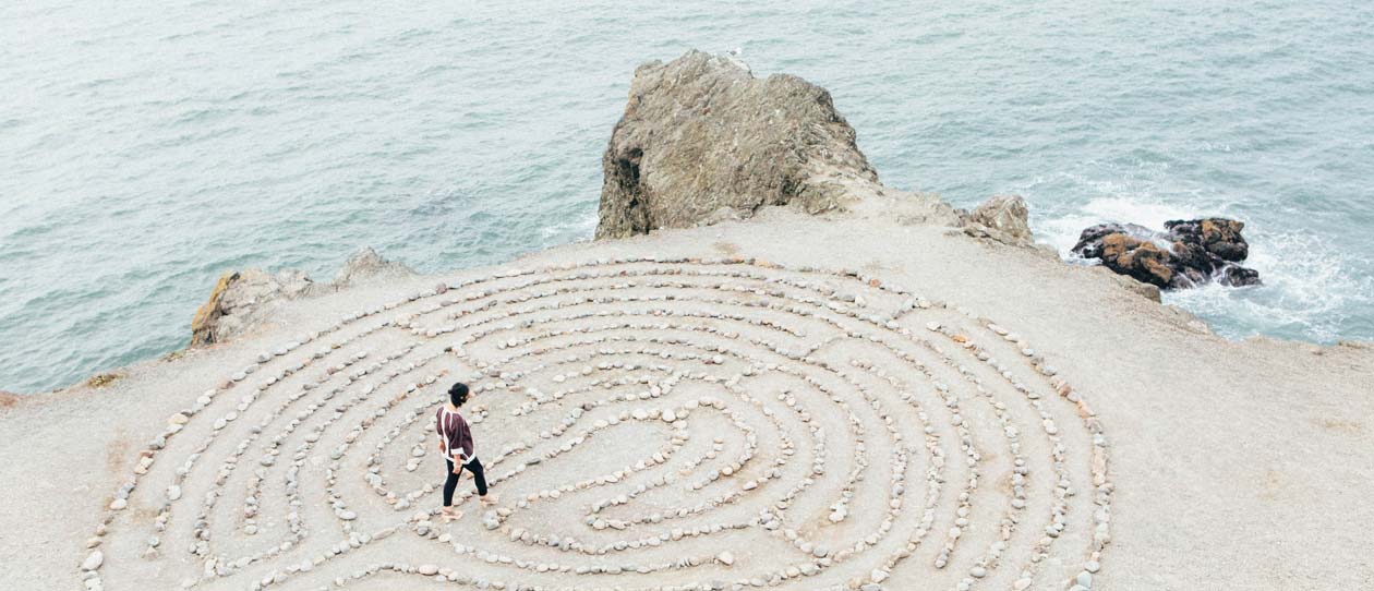 Woman walking through a labyrinth rock pattern on the sand at the coast