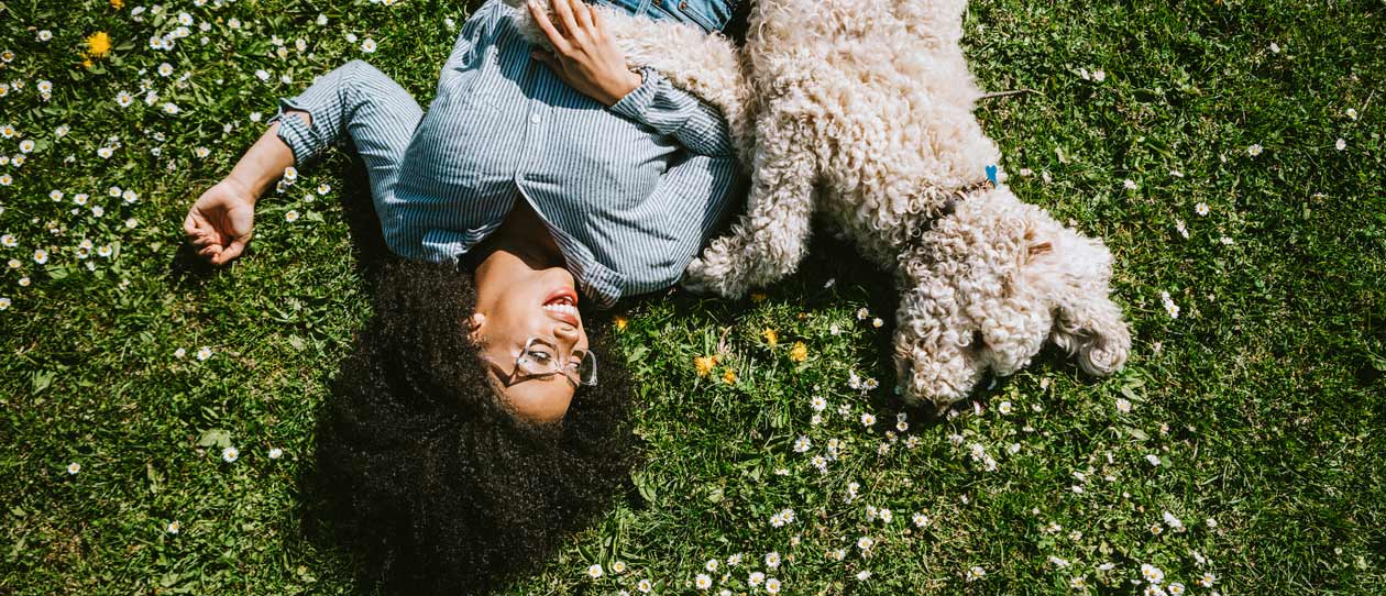 A happy young adult woman enjoys time at a park with her standard poodle, running, playing, and relaxing with the dog.