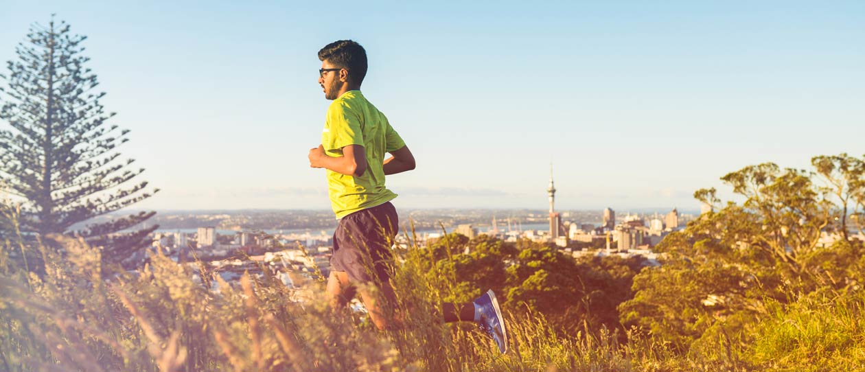 Man running on a hill in Auckland New Zealand with Sky Tower in background